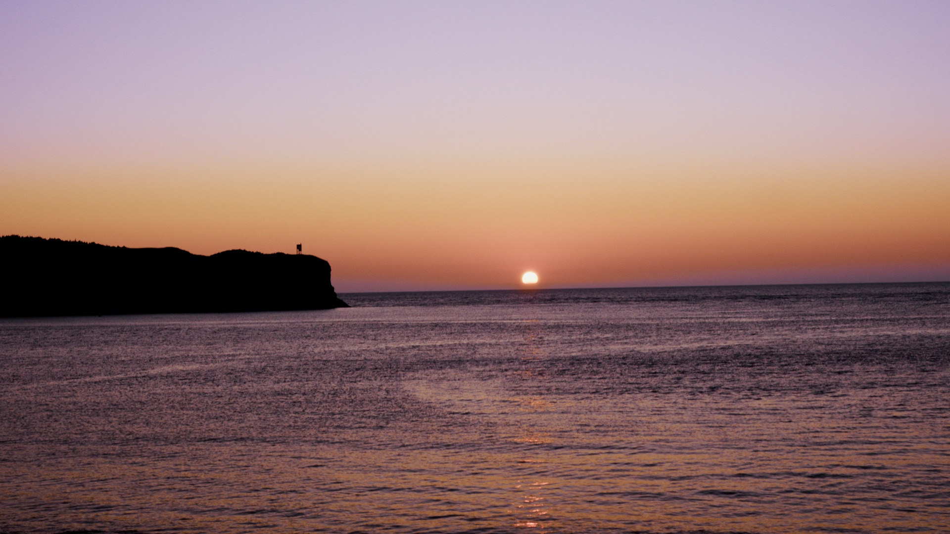 A low sun over the ocean beside a dark coastal cliff in Newfoundland.